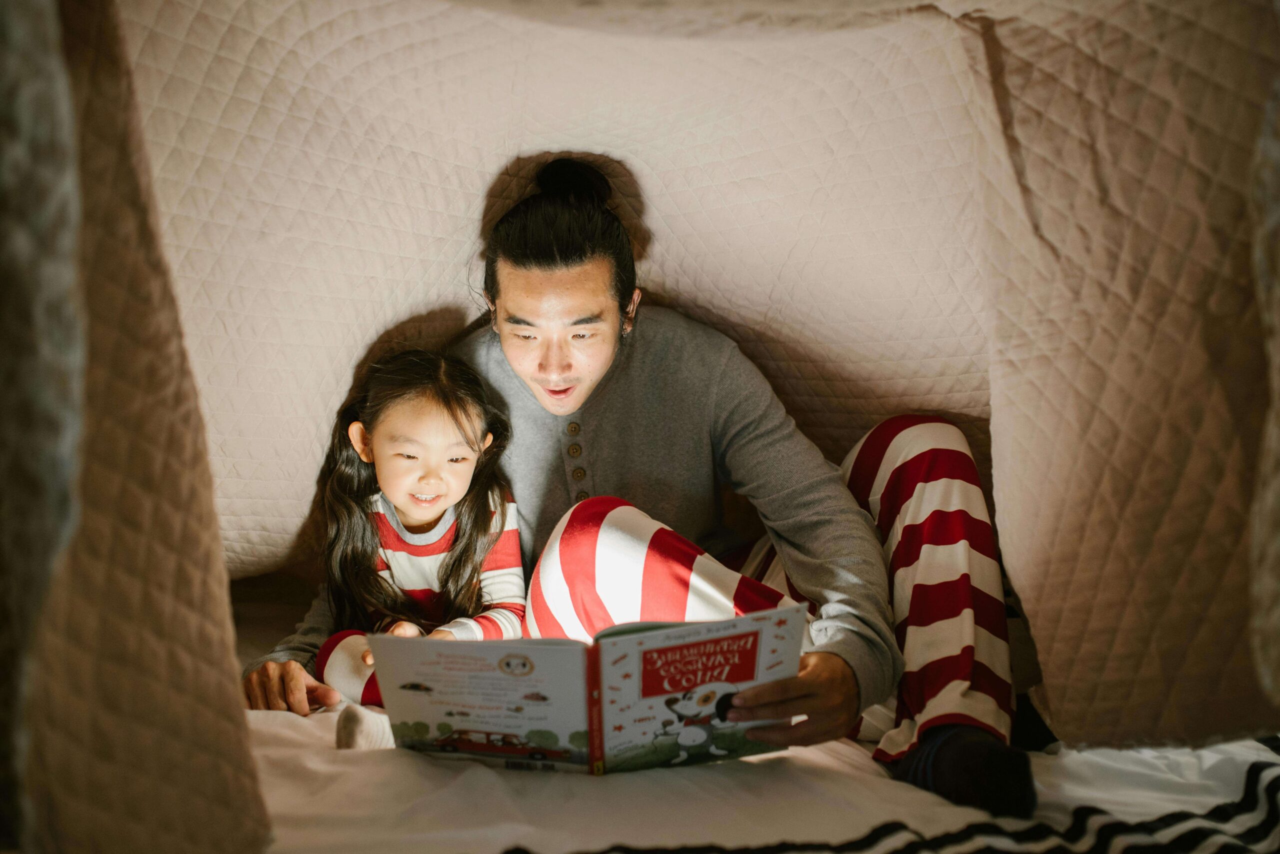 Father and daughter reading a children's picture book in a makeshift tent in the house