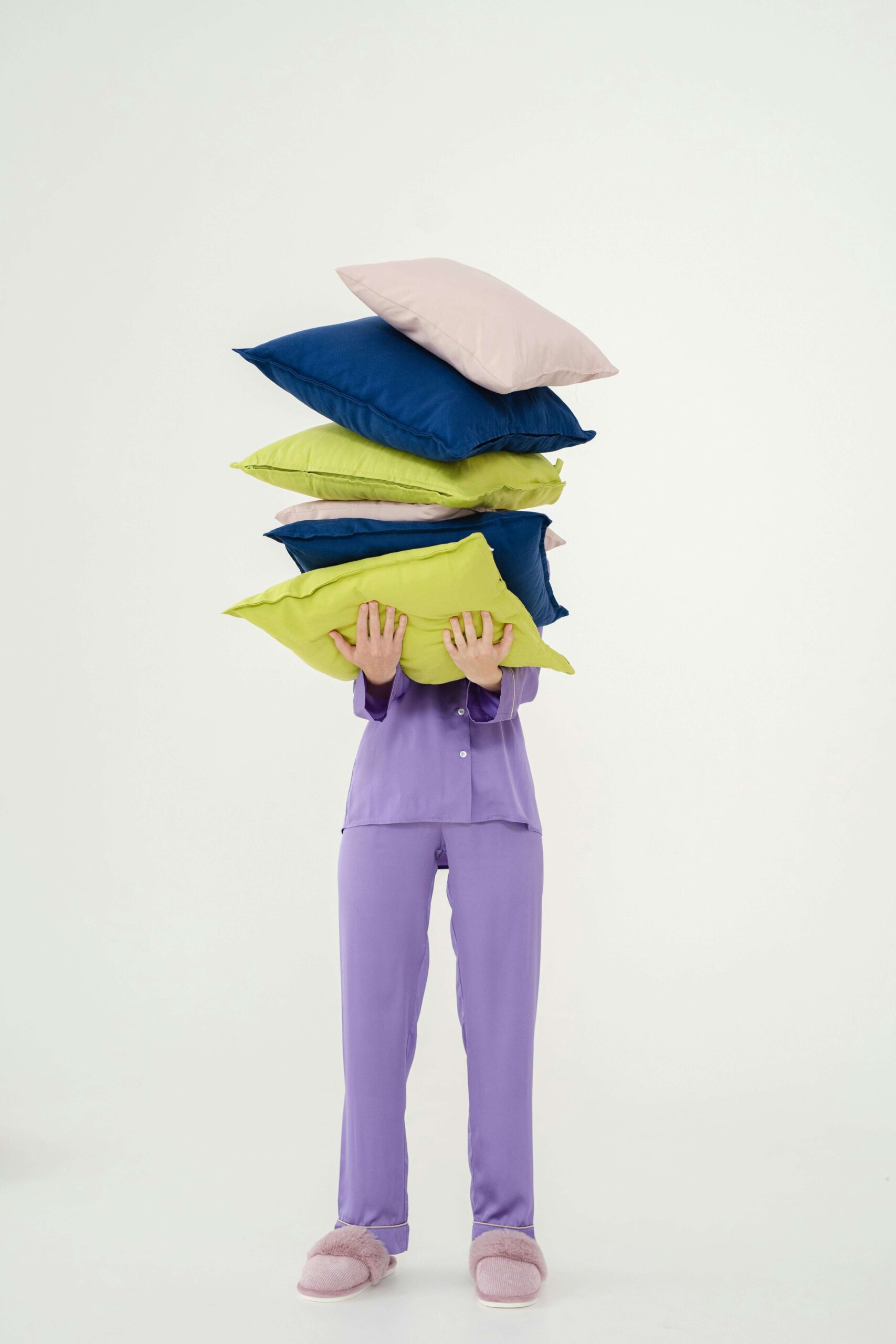 Person in pajamas carrying a stack of pillows