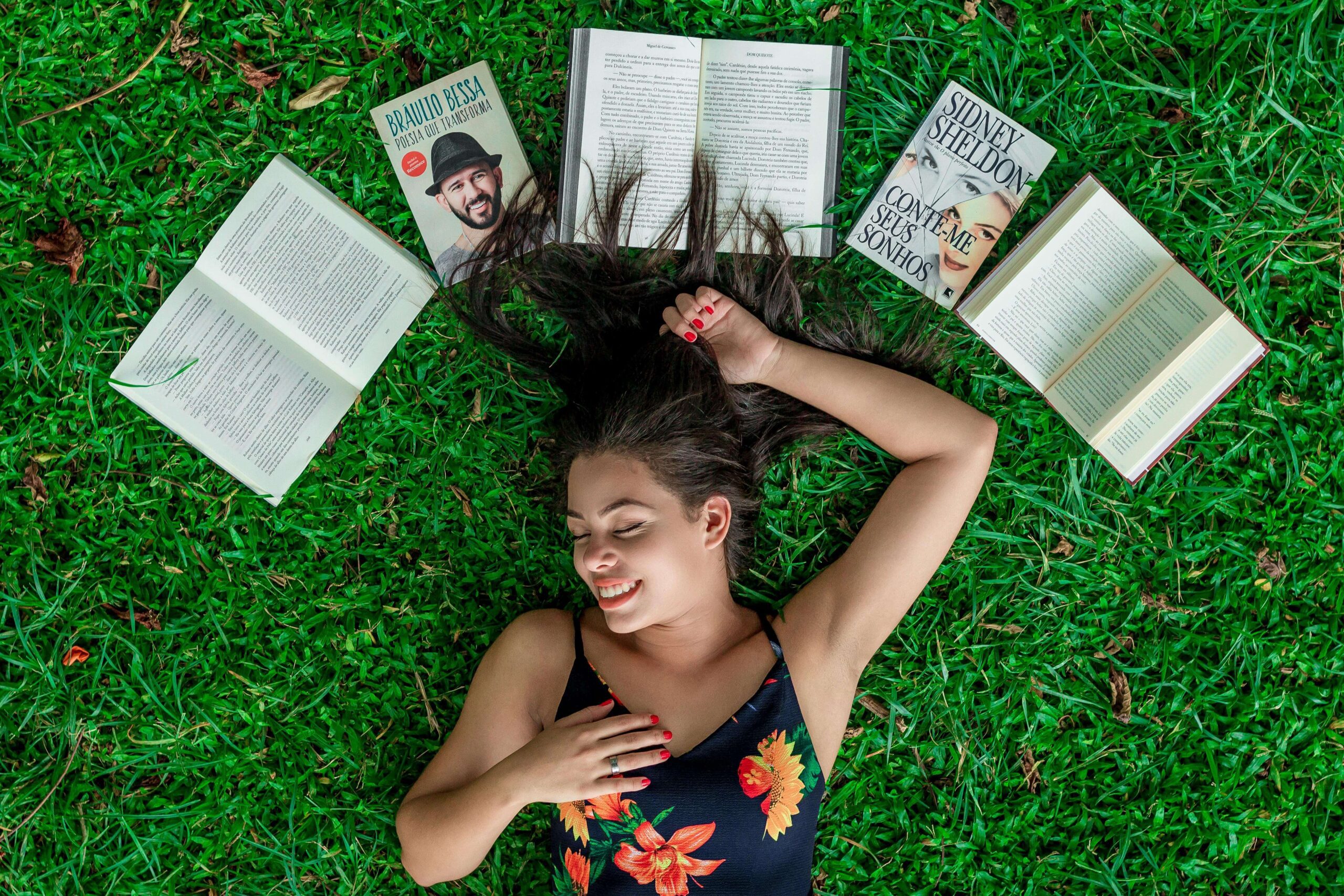 bool lover lying on the grass with her favorite books lined up above her