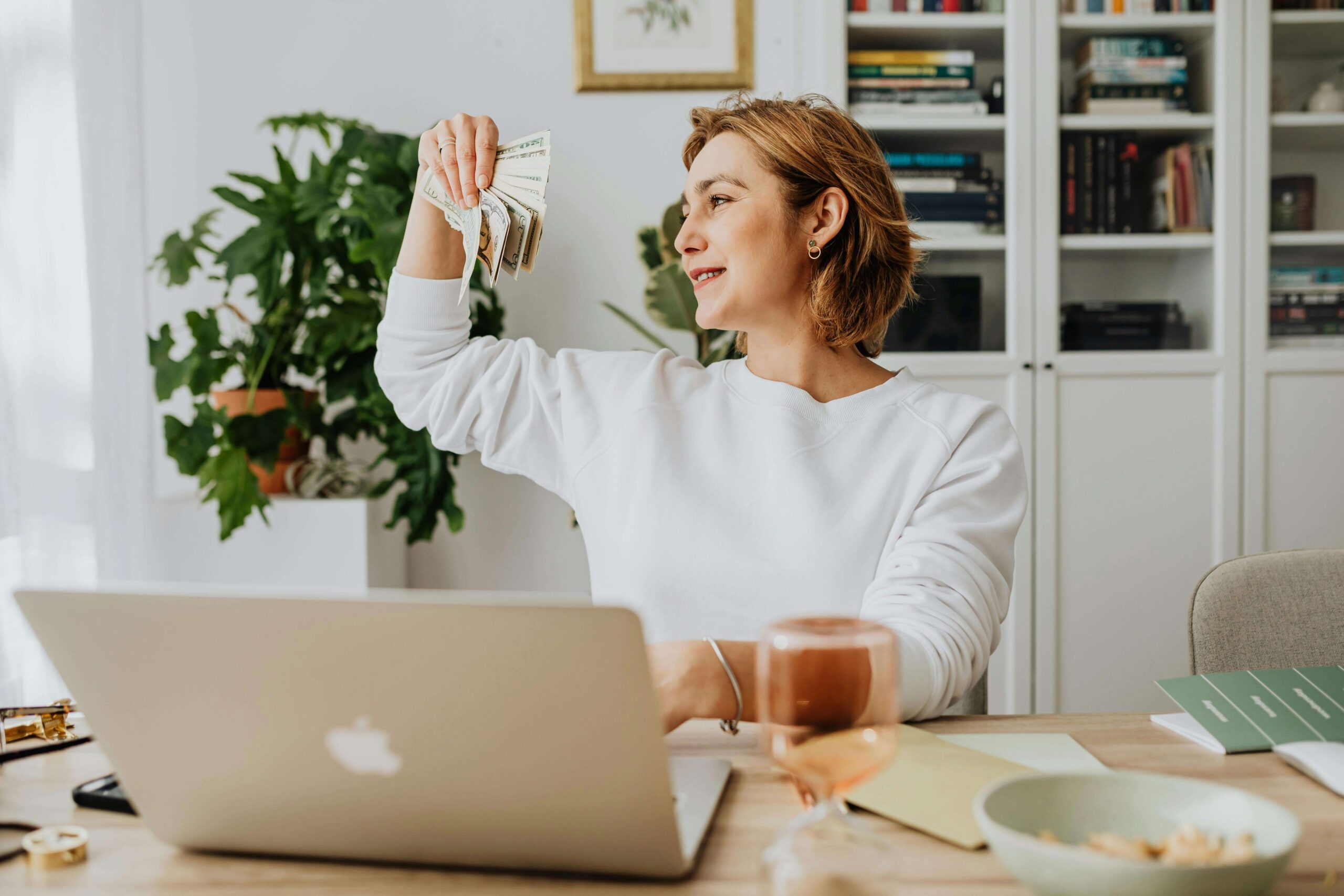 female author holding money in front of her laptop