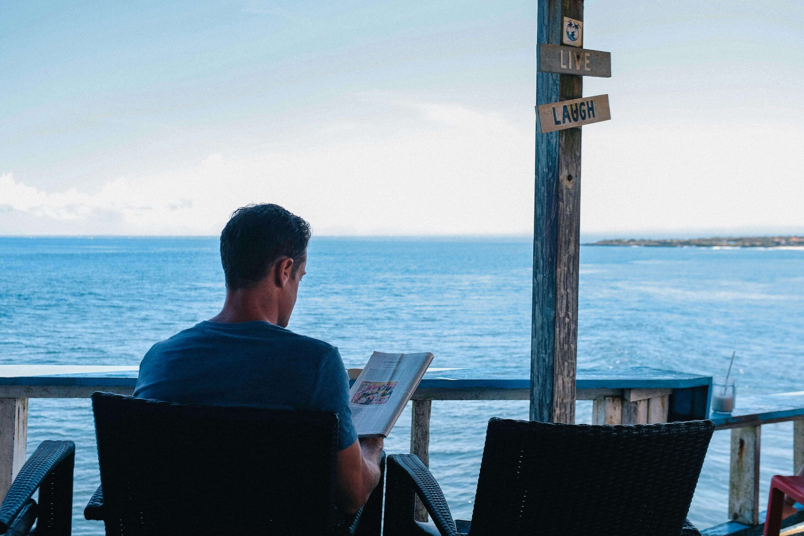man reading a book on a deck in front of the sea