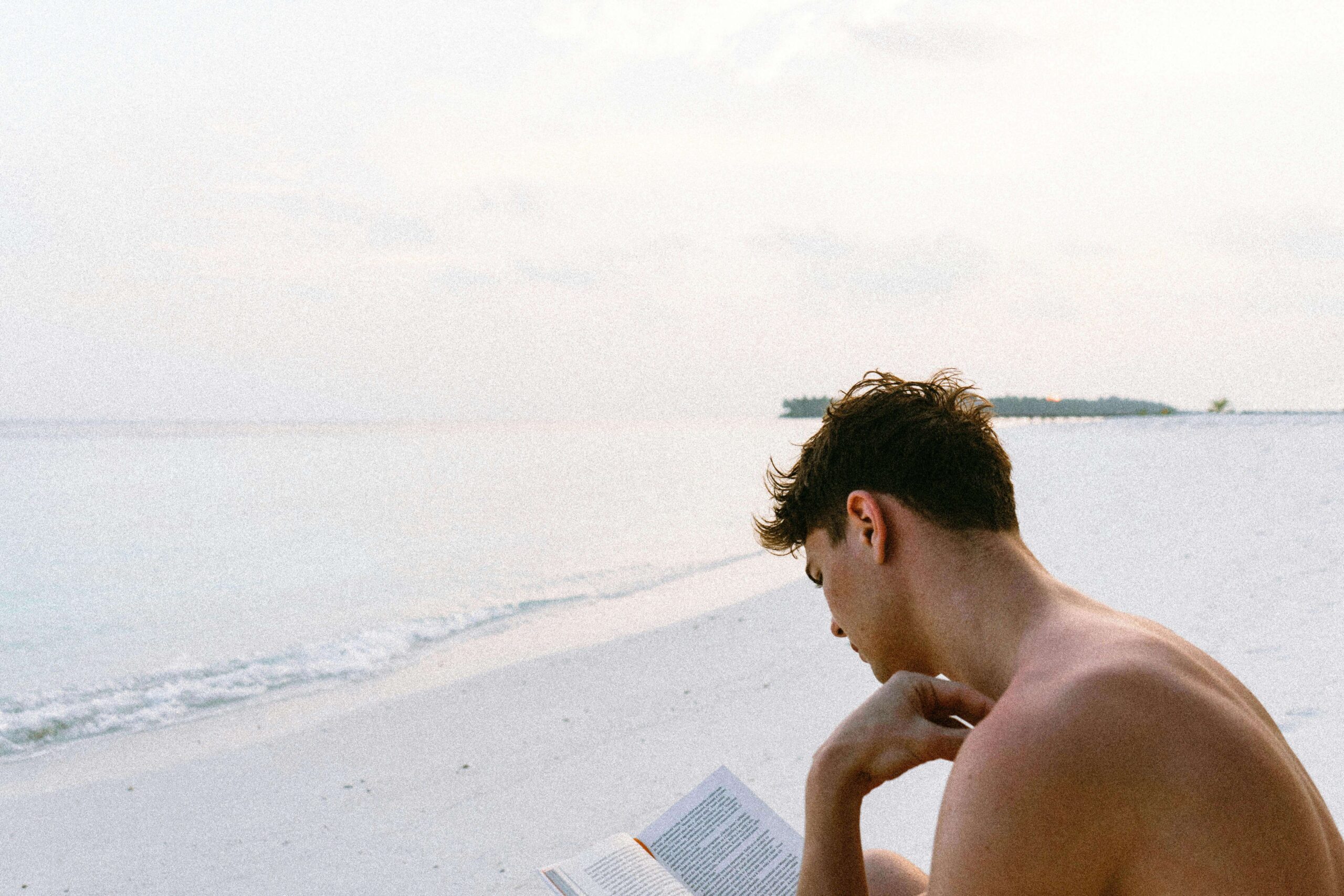 man reading a book by the beach